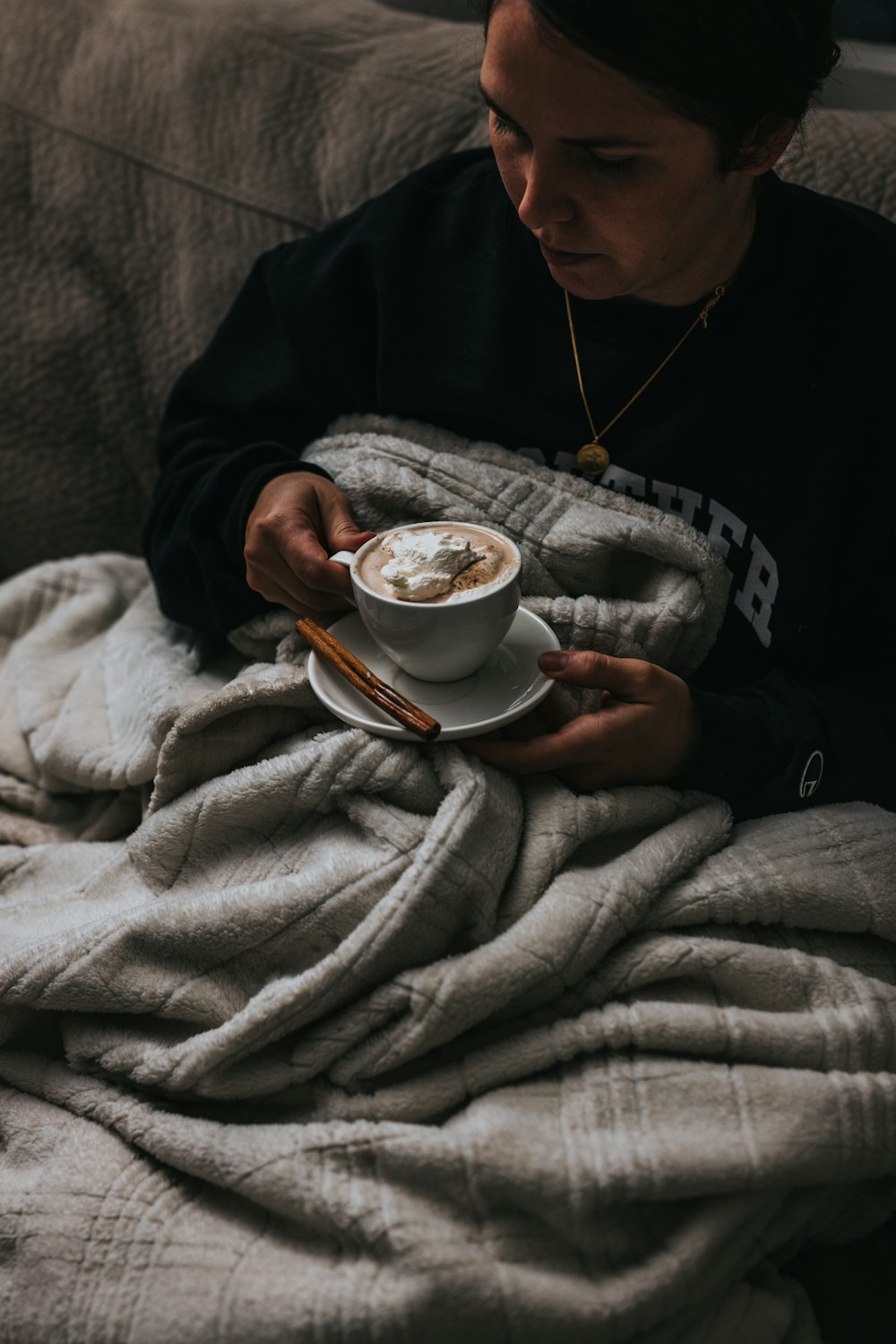 personne en pull noir tenant une tasse de thé en céramique blanche