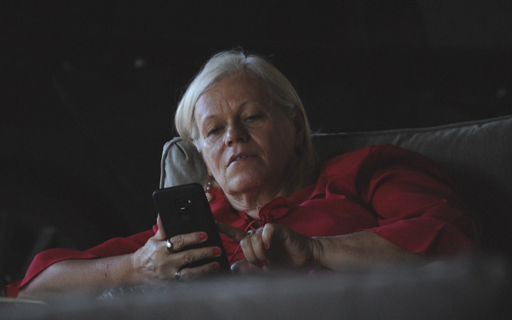 woman in red long sleeve shirt holding black smartphone