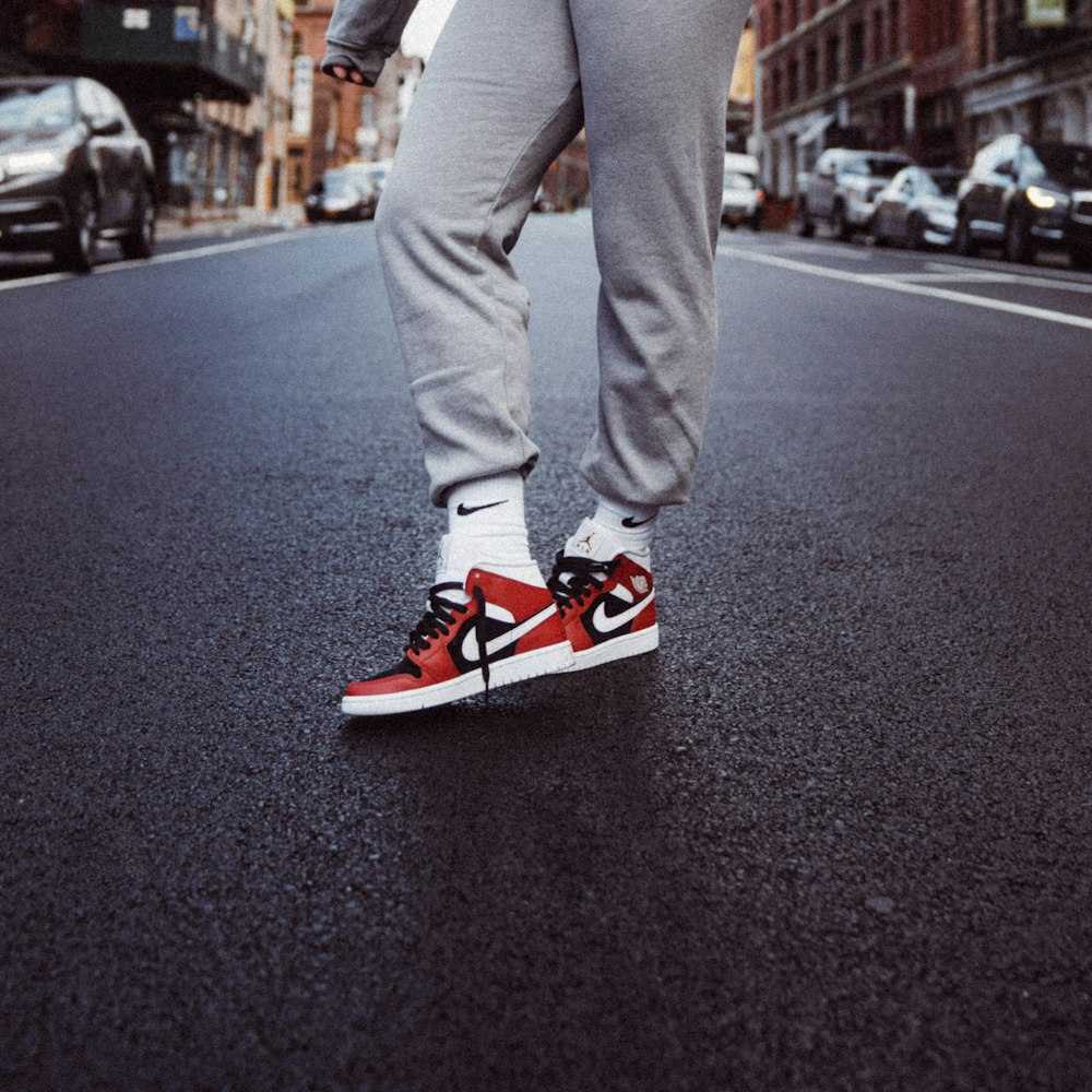 person in gray pants and red nike sneakers standing on gray asphalt road during daytime