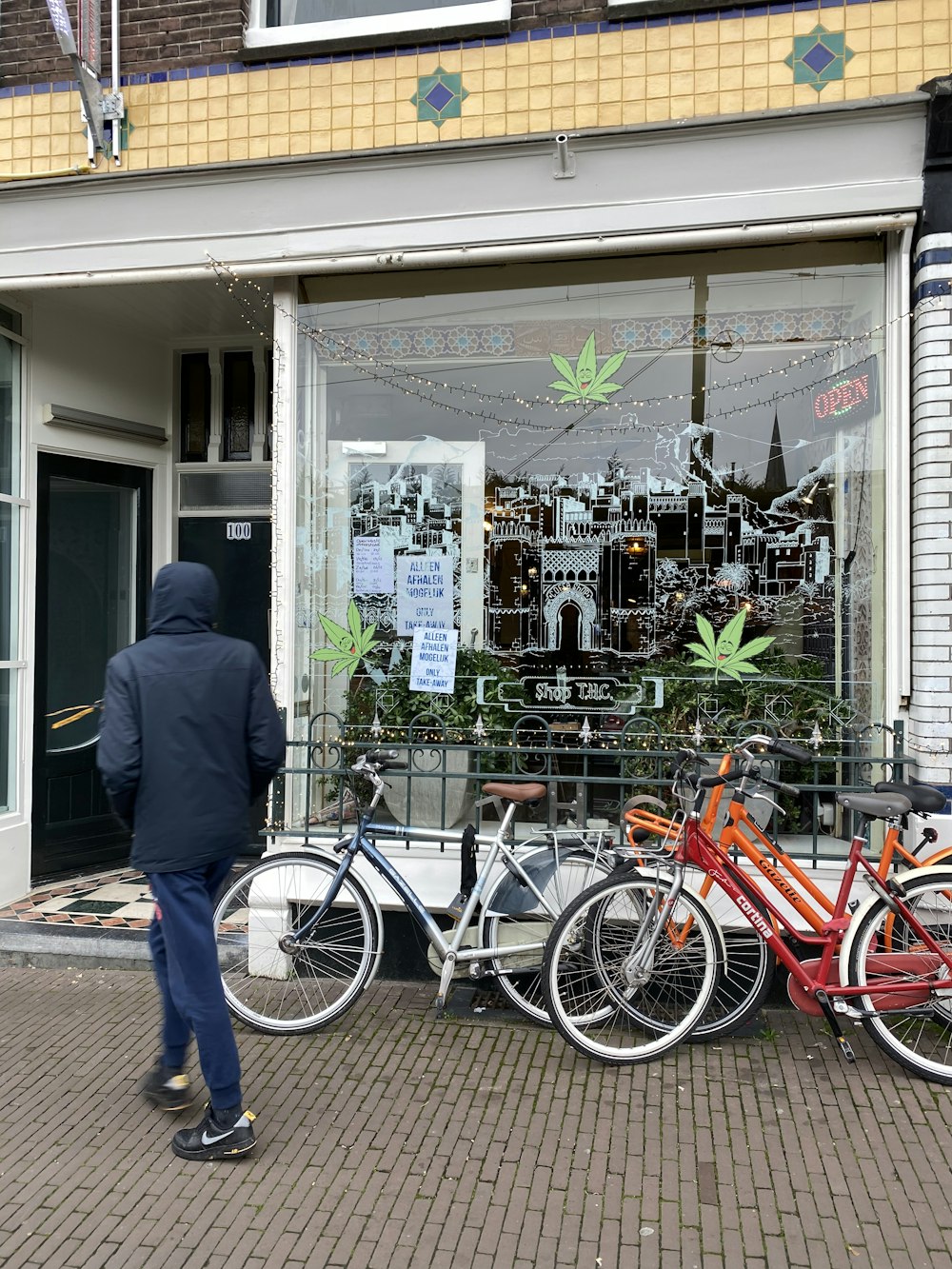 man in black jacket and blue denim jeans standing beside red city bicycle