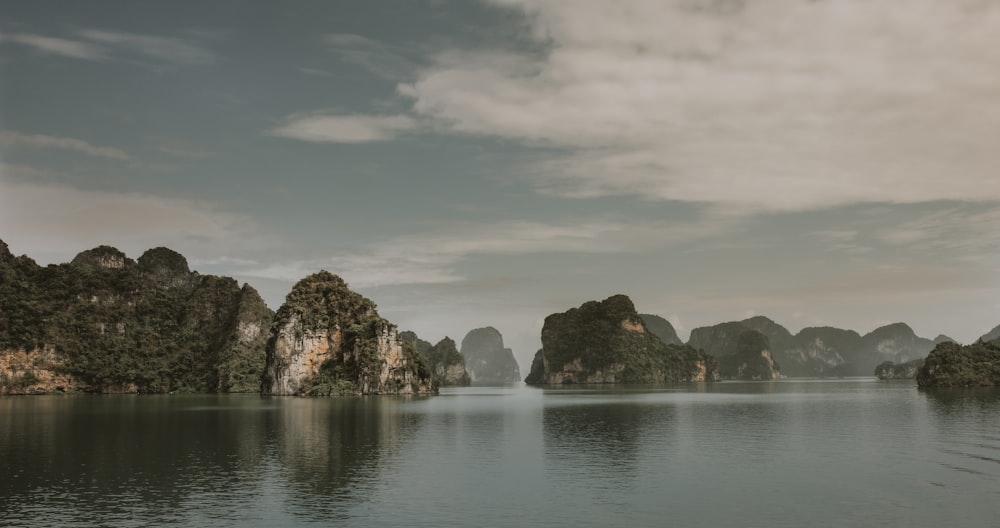 gray and black rocky mountain beside body of water under cloudy sky during daytime