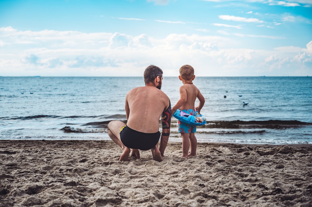 Hombre en pantalones cortos negros sosteniendo un cubo de plástico azul en la playa durante el día