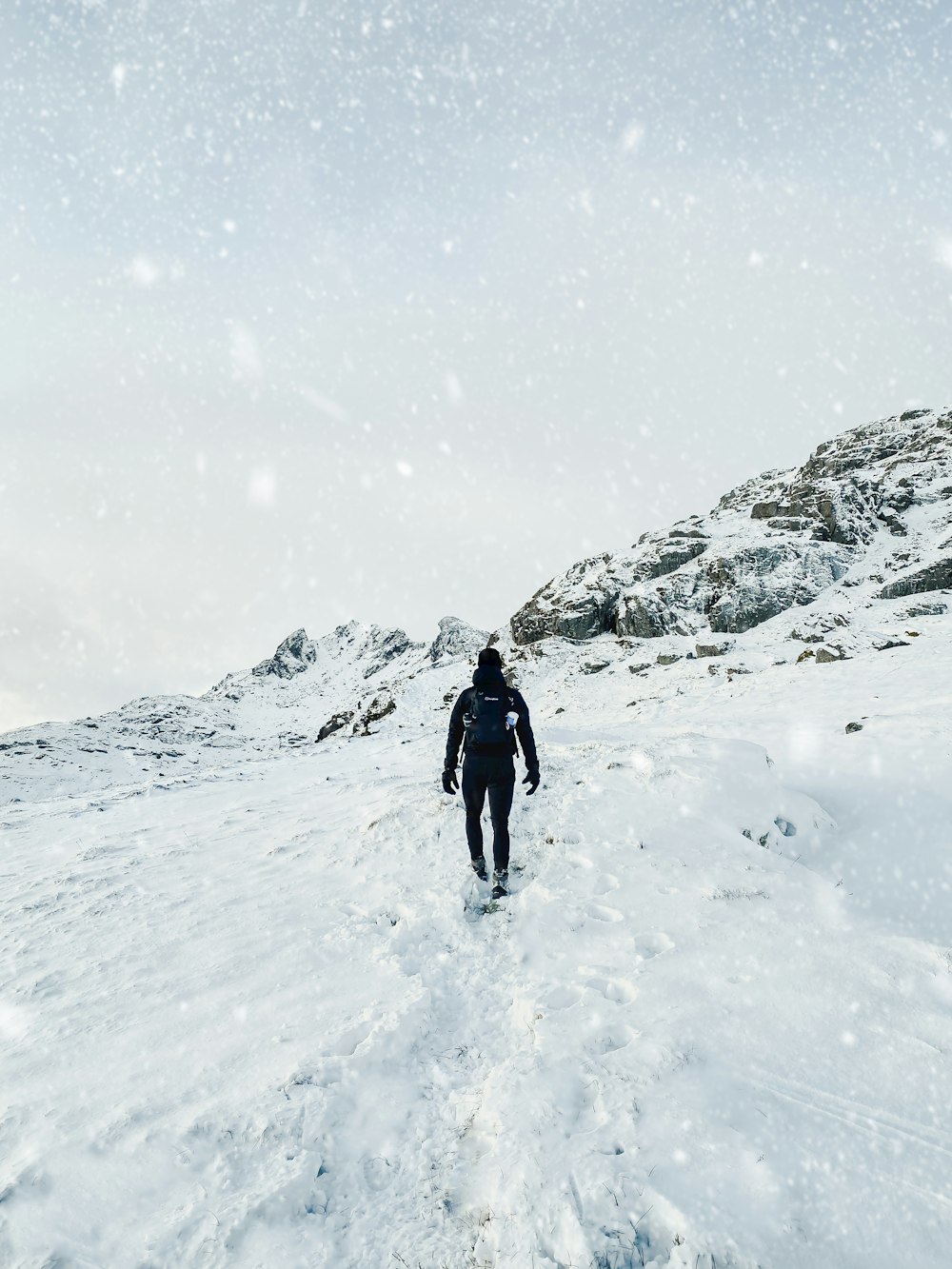昼間に雪に覆われた地面を歩く黒いジャケットの人