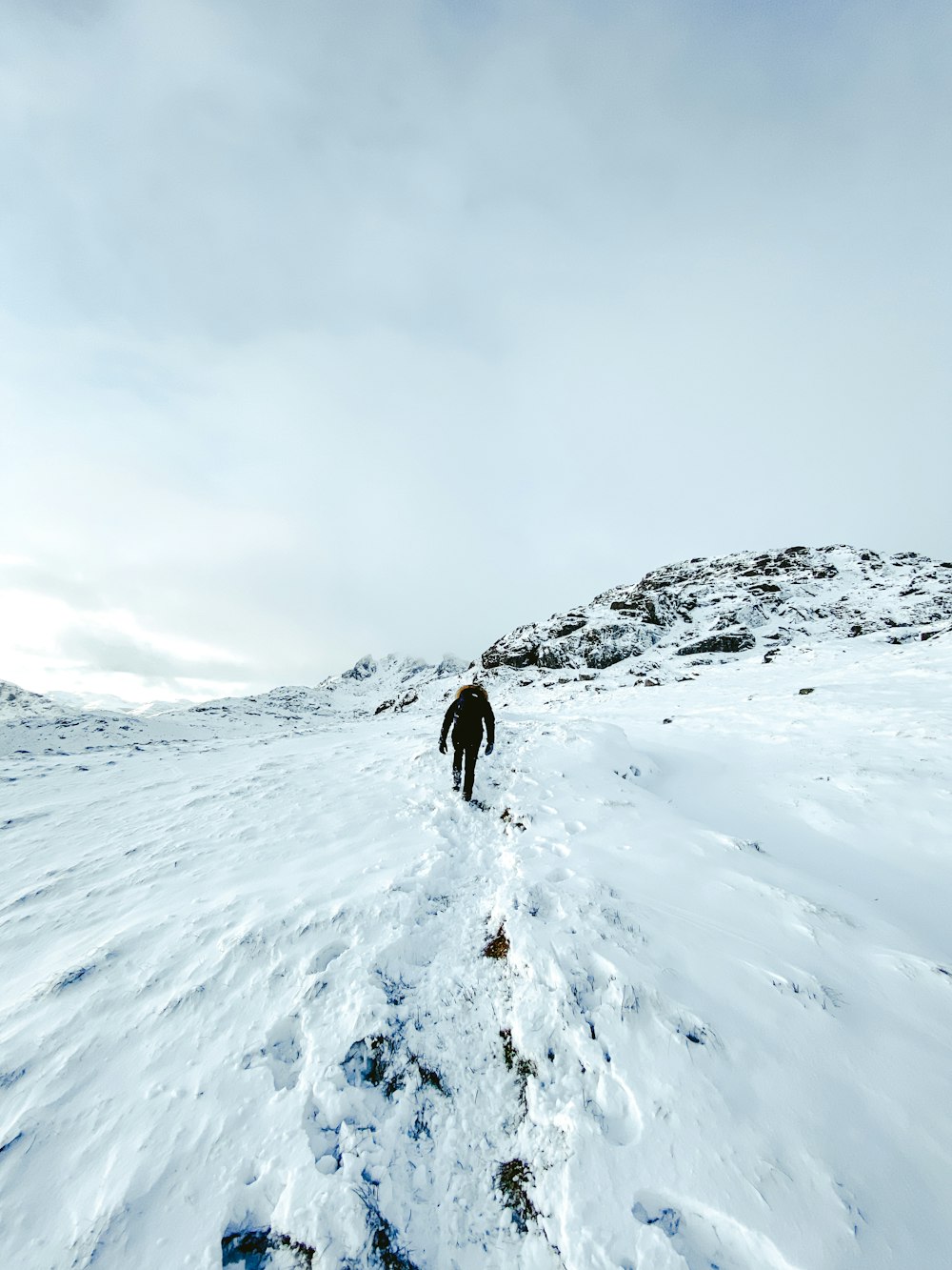 昼間、雪に覆われた山の上に立つ黒いジャケットを着た人