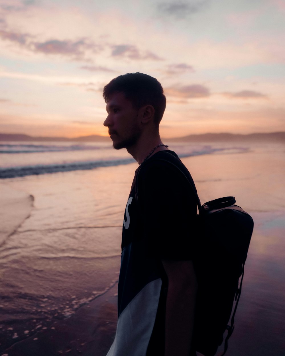 man in black shirt standing on beach during sunset