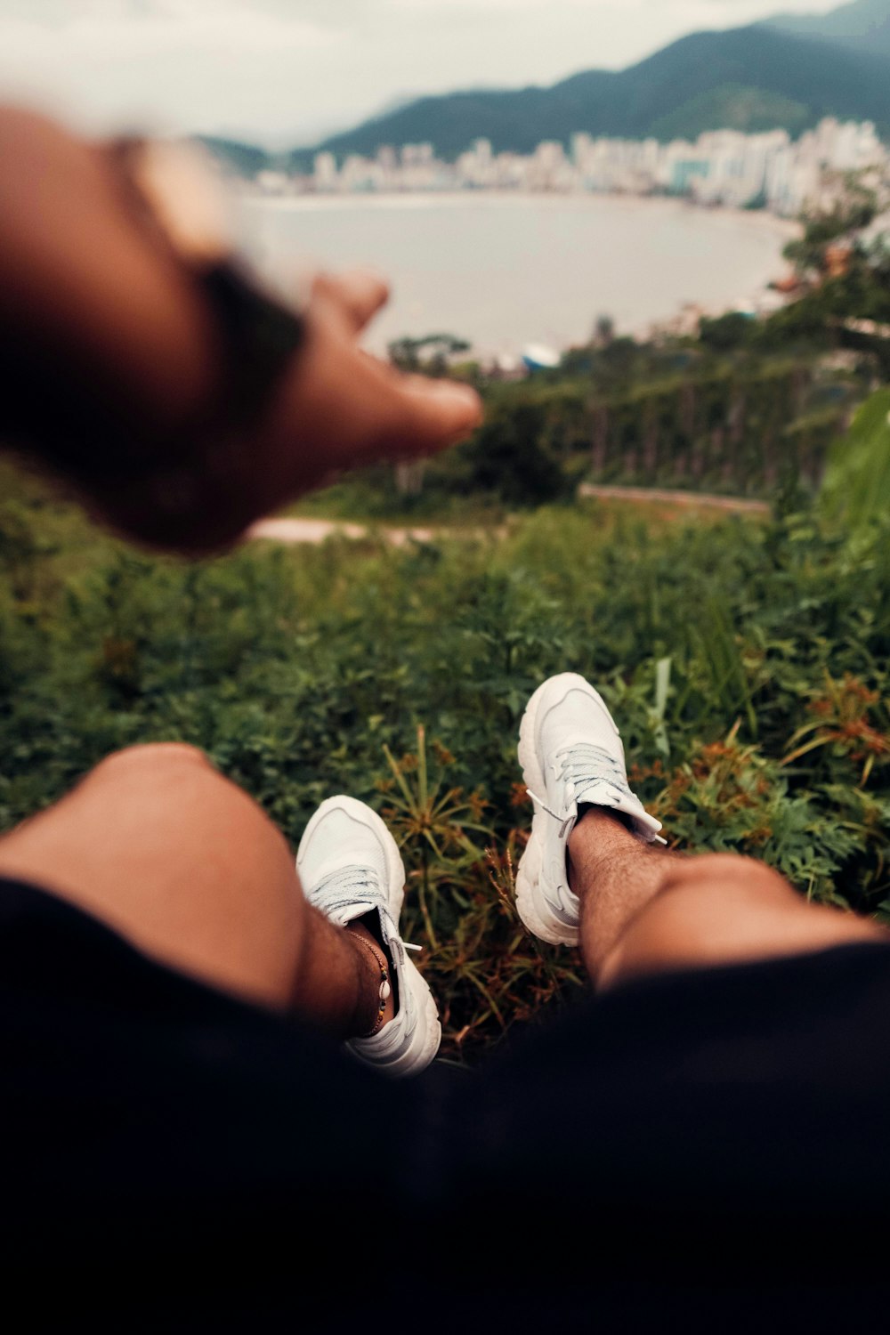 person in white sneakers sitting on grass field during daytime