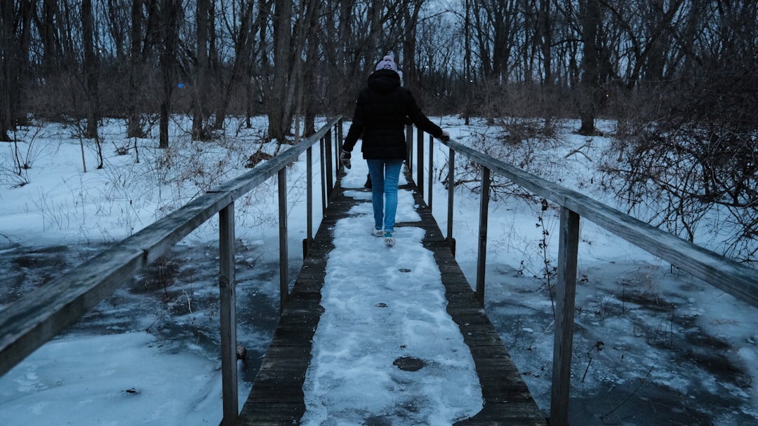 person in black jacket walking on snow covered bridge during daytime