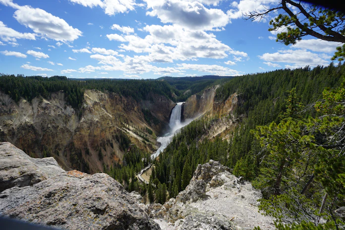waterfalls in the middle of green trees under blue sky and white clouds during daytime