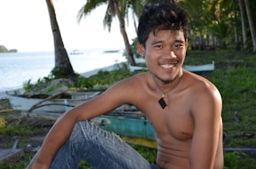topless man sitting on blue towel near swimming pool during daytime