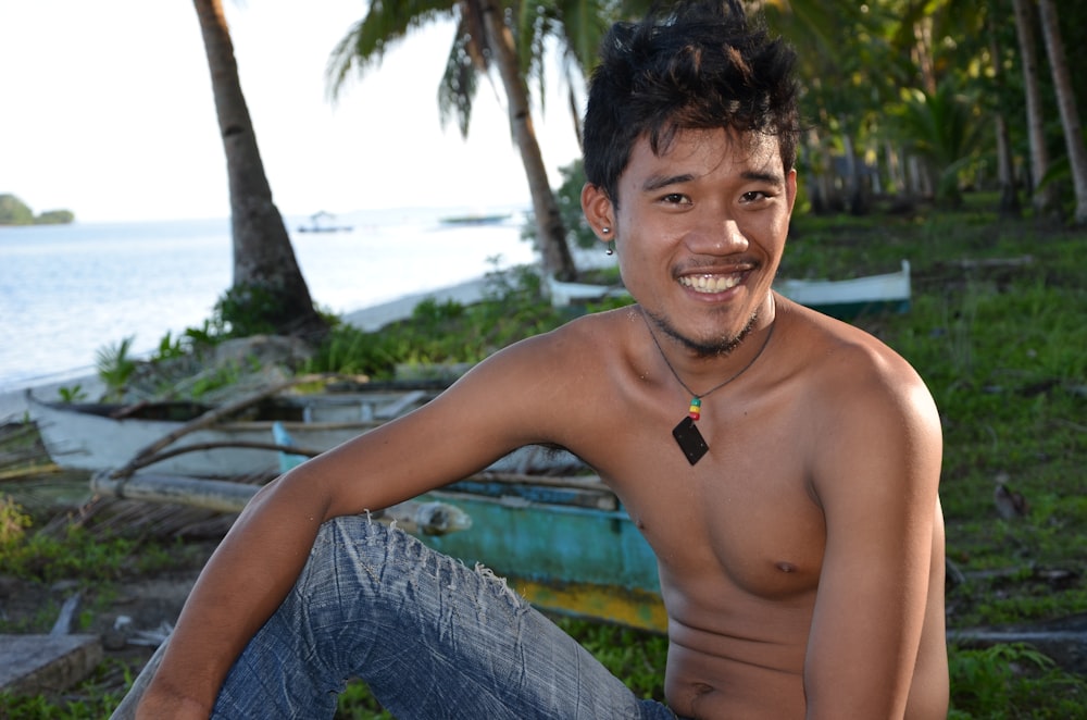 topless man sitting on blue towel near swimming pool during daytime