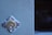 A close-up view of a metallic door lock set in a painted surface, with visible scratches and wear on the paint. To the right, there is a dark glass pane.