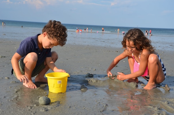 Kids building a sandcastle at the beach with colorful buckets and shovels