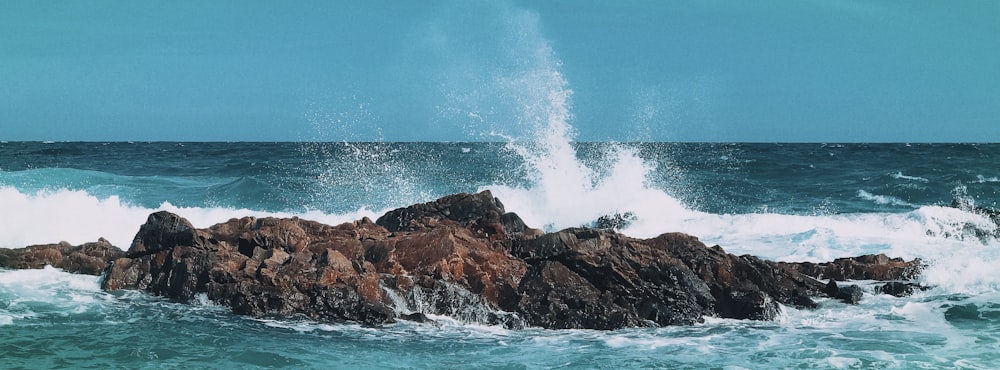 ocean waves crashing on brown rock formation under blue sky during daytime