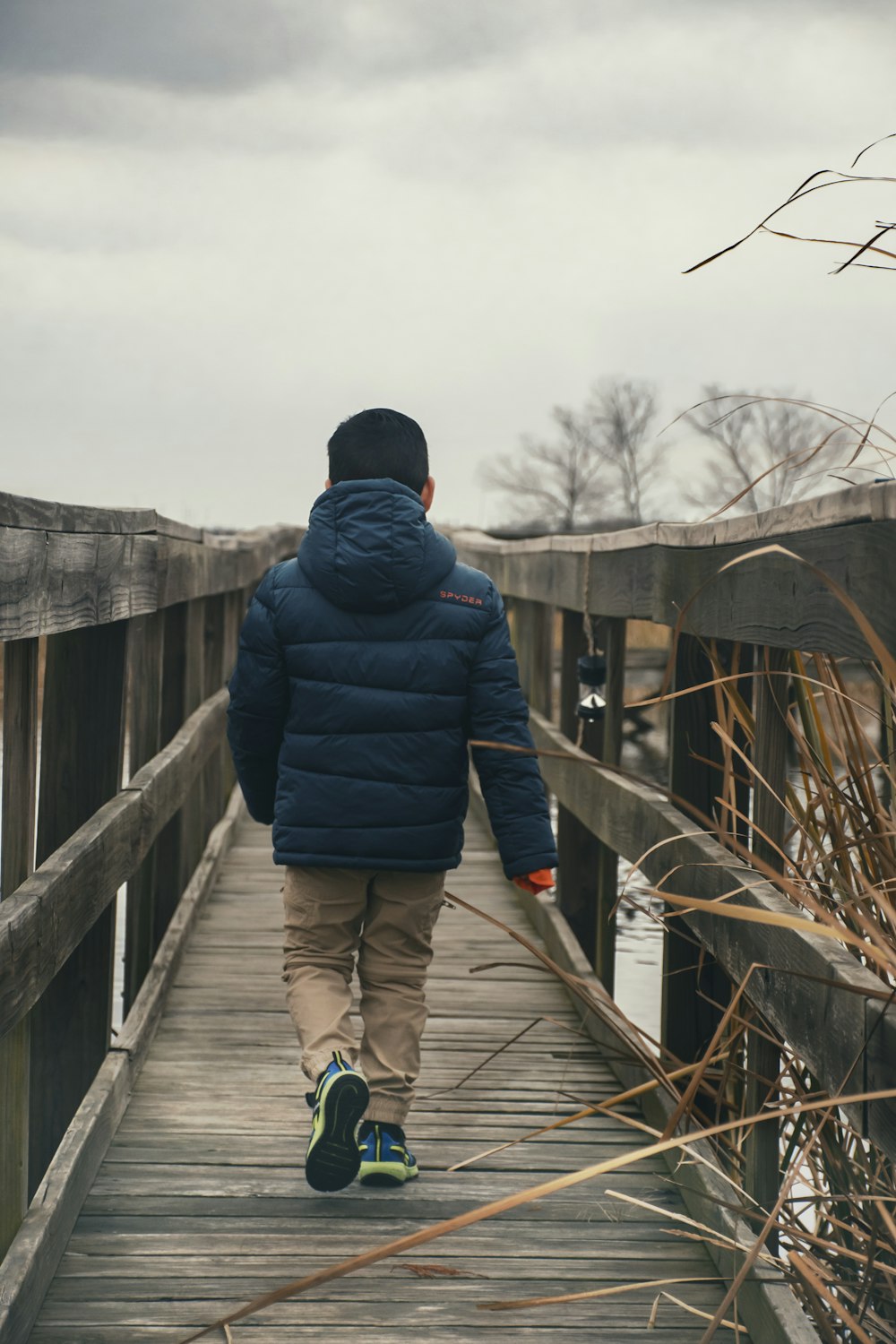 person in black jacket and black pants walking on wooden bridge