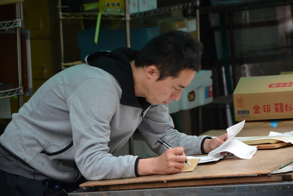 man in gray hoodie writing on white paper