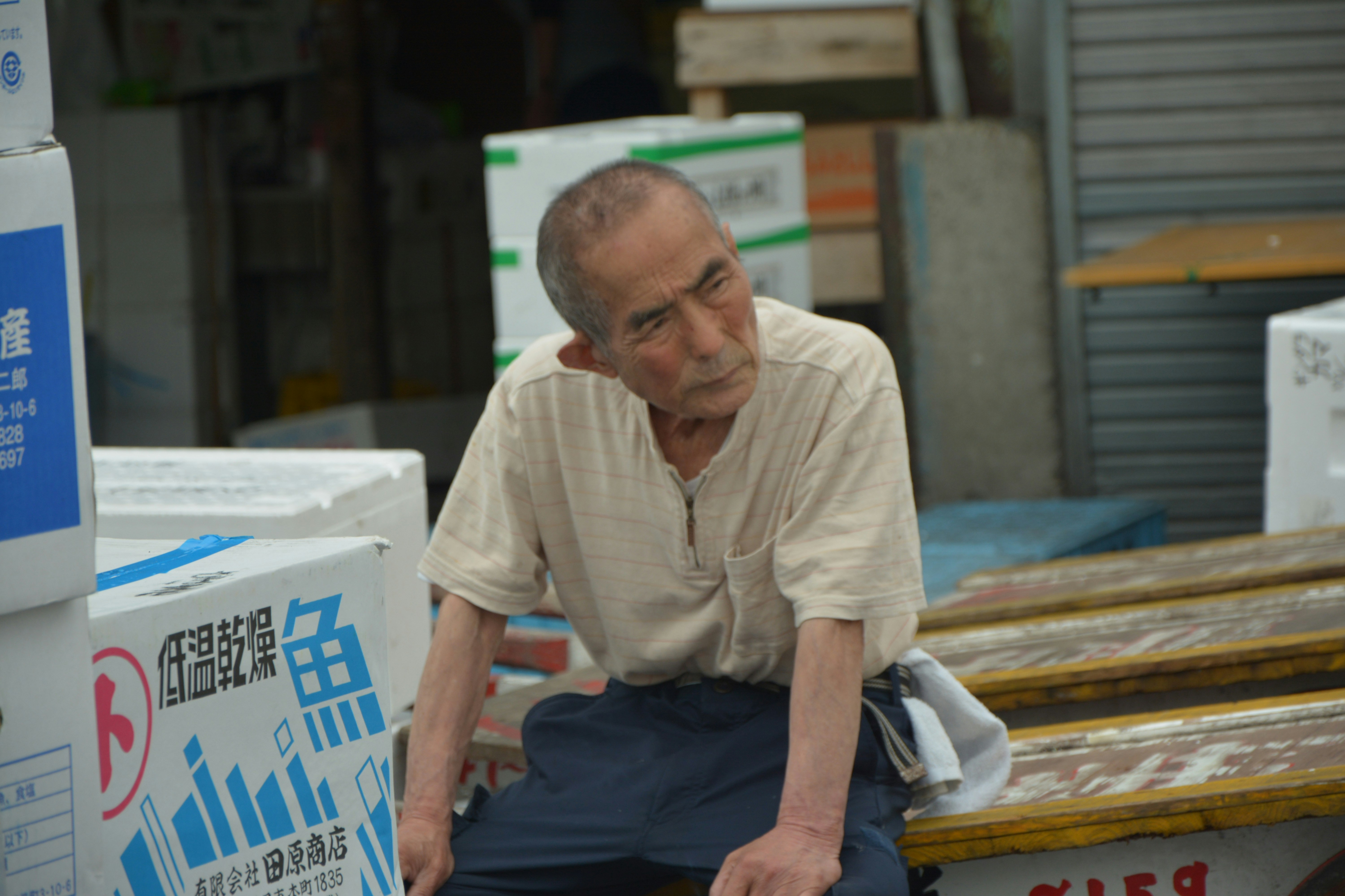 Old Japanese workman resting on boxes in the fish market