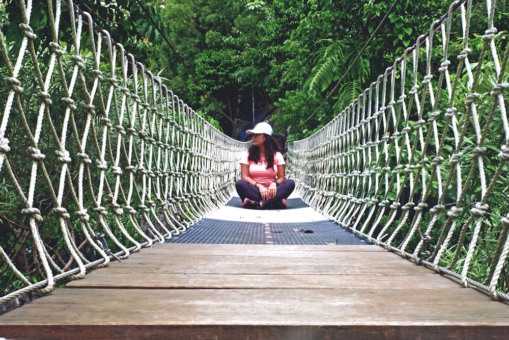 woman in black tank top sitting on brown wooden bridge during daytime