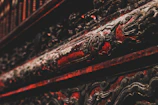 Intricate, ornate carvings with a dark and rich red finish, suggestive of traditional craftsmanship, embellished with darkened, possibly metal or wood, accents.