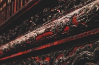 Intricate, ornate carvings with a dark and rich red finish, suggestive of traditional craftsmanship, embellished with darkened, possibly metal or wood, accents.