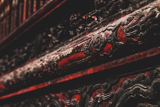 Intricate, ornate carvings with a dark and rich red finish, suggestive of traditional craftsmanship, embellished with darkened, possibly metal or wood, accents.