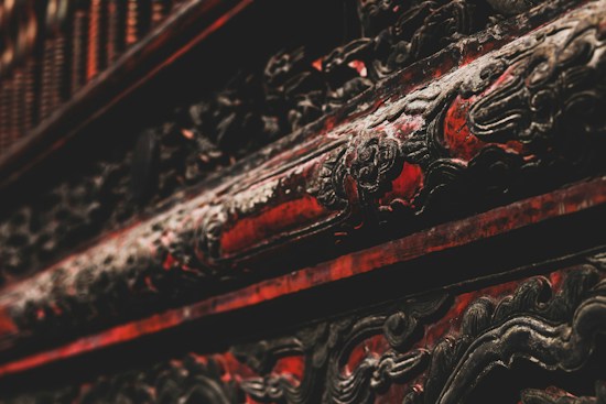 Intricate, ornate carvings with a dark and rich red finish, suggestive of traditional craftsmanship, embellished with darkened, possibly metal or wood, accents.