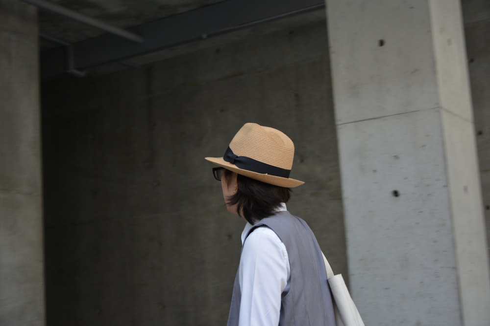 woman in white long sleeve shirt wearing brown hat standing near white wall