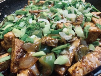 A close-up view of a dish featuring cubed tofu pieces cooked with chopped green onions and bell peppers in a savory sauce.