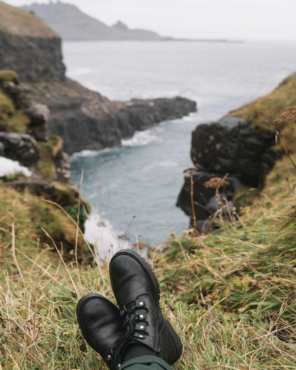 person wearing black leather shoes on brown rock near body of water during daytime