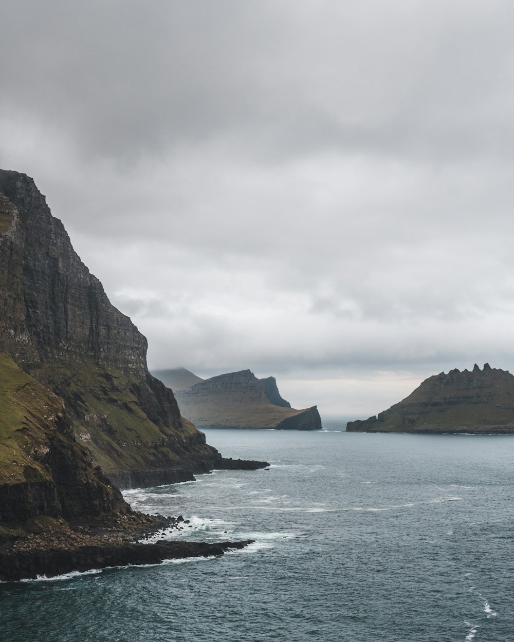 brown and green mountain beside body of water under white cloudy sky during daytime