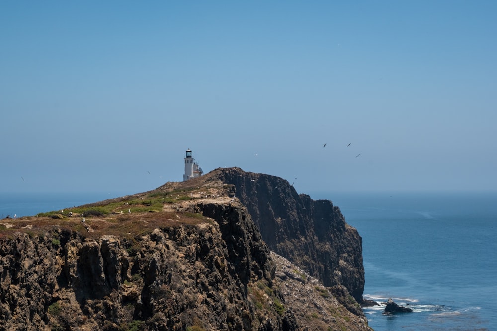 farol branco no topo da montanha marrom perto do corpo de água durante o dia