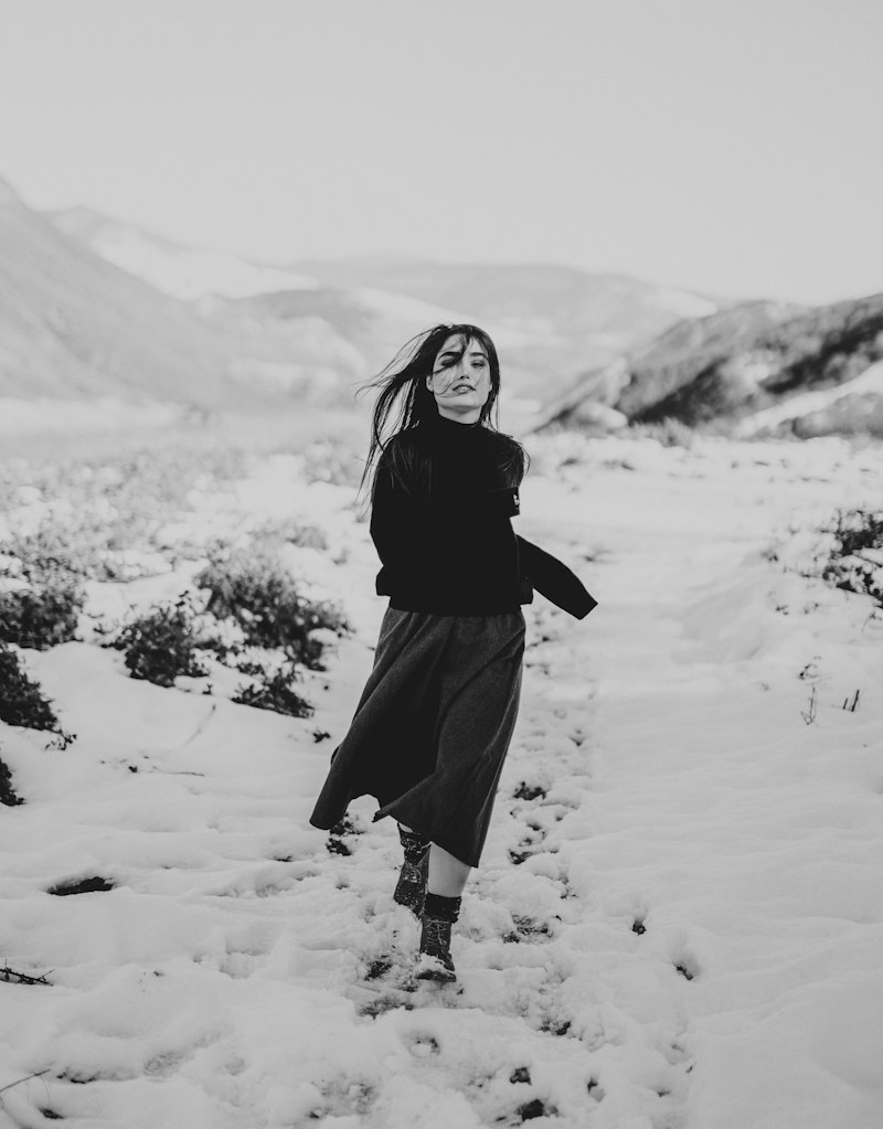 Femme en jupe longue et pull noir dans la neige