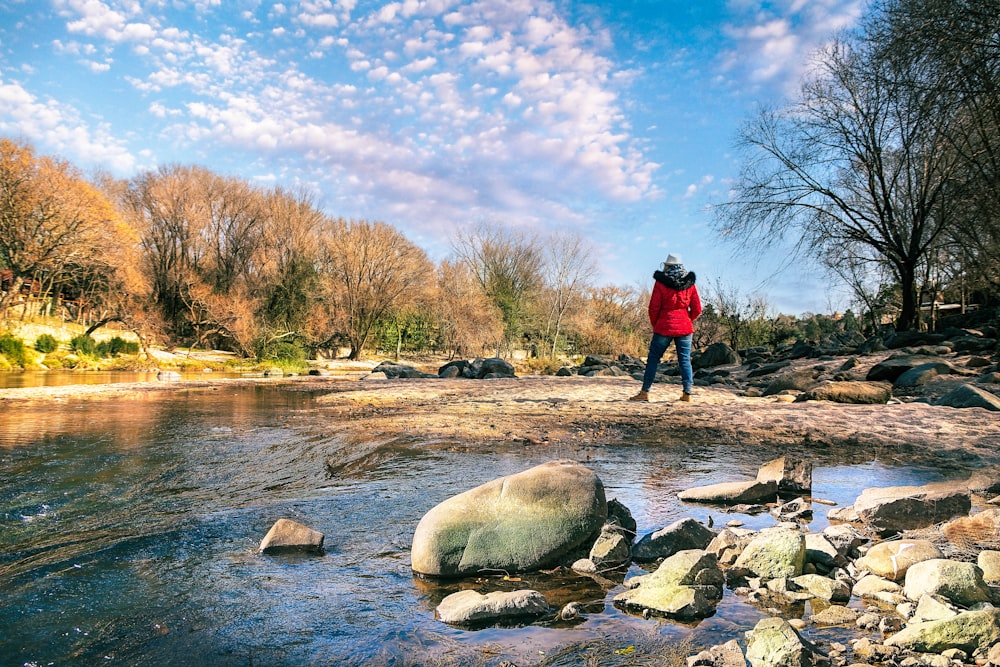 person in red jacket standing on rock near river during daytime