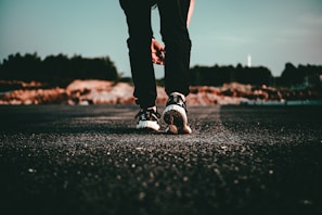 Side view of a person walking in black Leviticus Wear joggers and sneakers on a dimly lit city sidewalk.