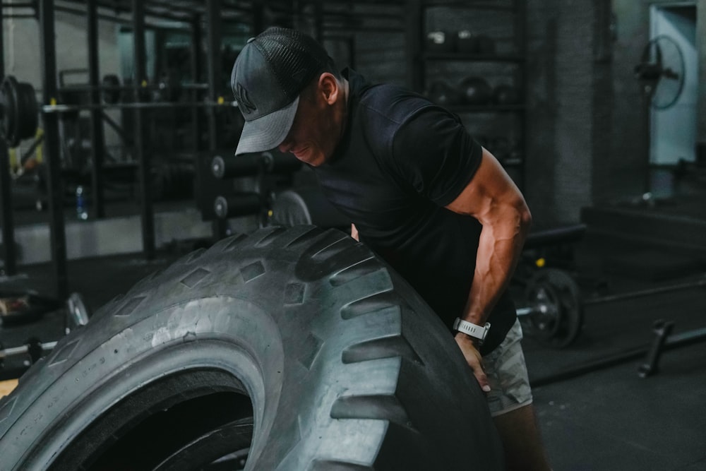 man in black t-shirt and black cap holding car wheel