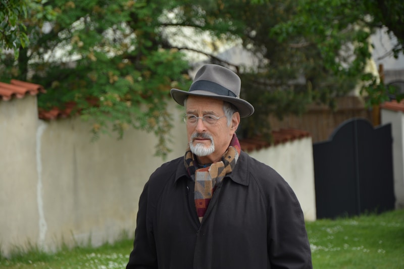 man in black jacket wearing black fedora hat standing on green grass field during daytime