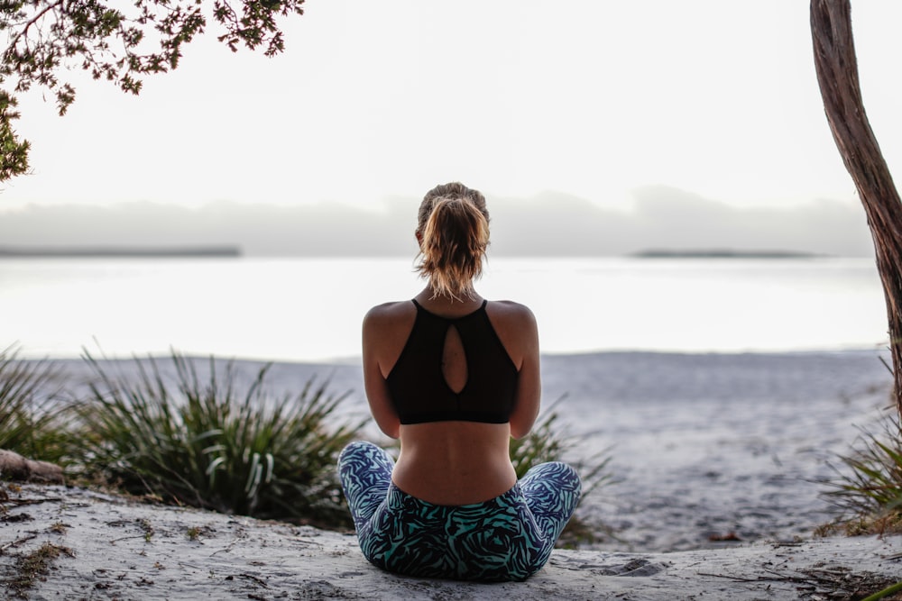 woman in black sports bra and blue white and black pants sitting on gray concrete pavement