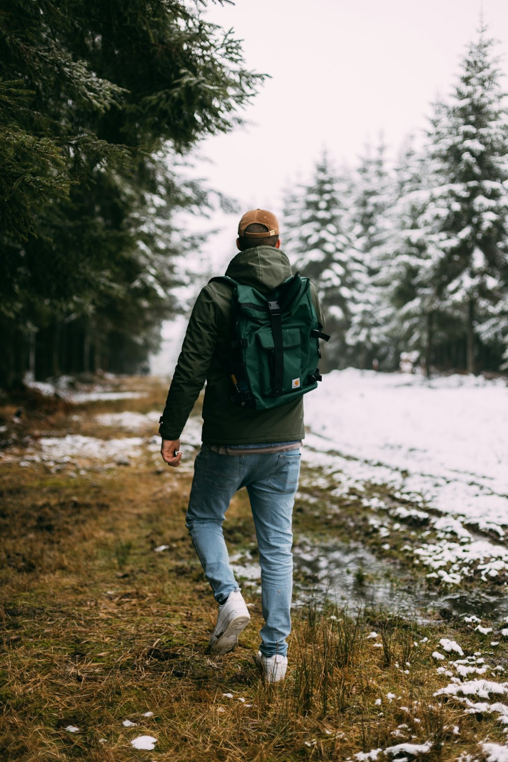 man in black jacket and blue denim jeans walking on snow covered ground during daytime