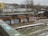 An urban setting features old brick structures covered in colorful graffiti and street art. Pipes run across the top of the structures, and a railway track is visible in the foreground. Snow is scattered on the ground, suggesting a cold season. In the background, there are residential buildings, some with trees bereft of leaves, adding to the wintery atmosphere.