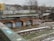An urban setting features old brick structures covered in colorful graffiti and street art. Pipes run across the top of the structures, and a railway track is visible in the foreground. Snow is scattered on the ground, suggesting a cold season. In the background, there are residential buildings, some with trees bereft of leaves, adding to the wintery atmosphere.