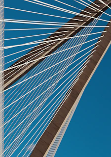 Close-up of a cable-stayed bridge's sleek cables stretching towards the sky against a bright blue backdrop.