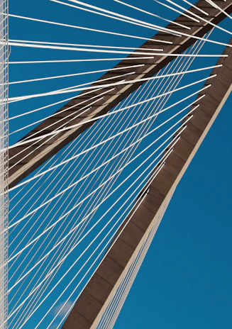 Close-up of a cable-stayed bridge's sleek cables stretching towards the sky against a bright blue backdrop.