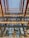 A multi-story glass building facade reflecting a pattern of vertical wooden beams and abstract shapes. The architecture features a grid-like window arrangement with large, reflective panes. Sunlight casts shadows and highlights across the structure, creating dynamic visual textures.