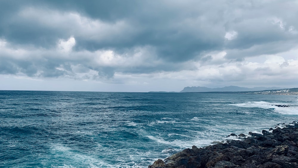 ocean waves crashing on rocky shore under white clouds during daytime