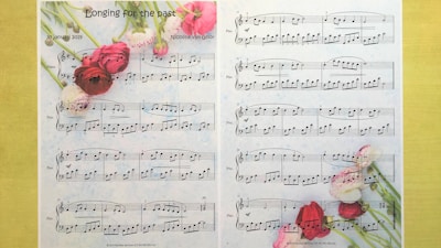 A sheet of piano music titled 'Longing for the past' composed by Nicoline van Goor. The sheet music is adorned with vibrant images of pink, red, and white flowers, which are positioned across the top and bottom of the page. The notation is clear and neatly arranged, indicating a piece composed on January 30, 2019.