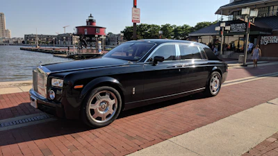 Shiny black car with spotless windows parked by a marina.