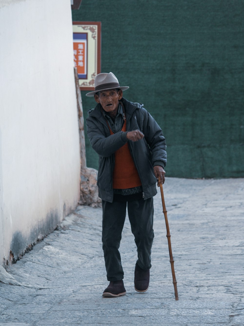 man in black jacket and black pants holding stick walking on sidewalk during daytime
