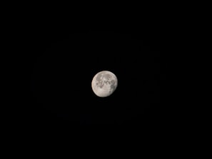 A well-defined image of the moon set against a stark black background. The lunar surface is partially illuminated, with visible craters and texture.