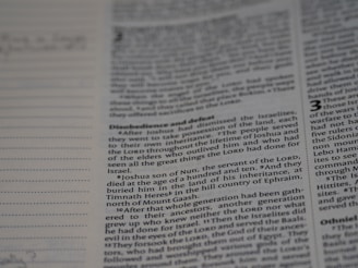 A close-up of a book page with text, focusing on a passage that mentions Joshua, the servant of the Lord, and his burial. The text discusses events related to the Israelites and includes religious themes. Dotted lines are visible on the left, possibly for notes or annotations.