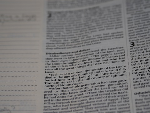 A close-up of a book page with text, focusing on a passage that mentions Joshua, the servant of the Lord, and his burial. The text discusses events related to the Israelites and includes religious themes. Dotted lines are visible on the left, possibly for notes or annotations.