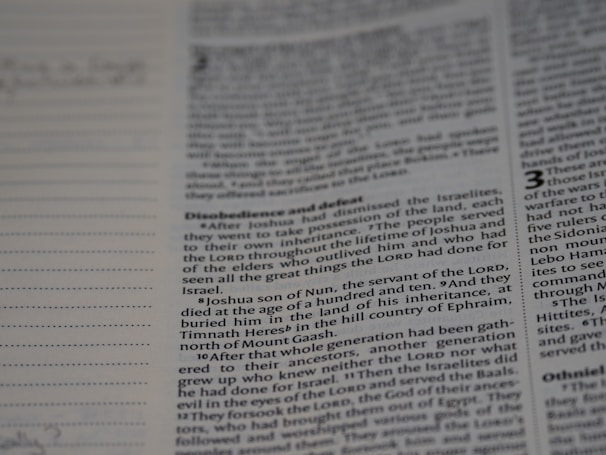 A close-up of a book page with text, focusing on a passage that mentions Joshua, the servant of the Lord, and his burial. The text discusses events related to the Israelites and includes religious themes. Dotted lines are visible on the left, possibly for notes or annotations.